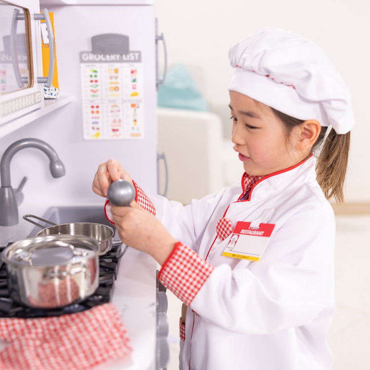 A kid playing with The Melissa & Doug Chef Role Play Costume Dress -Up Set With Realistic Accessories