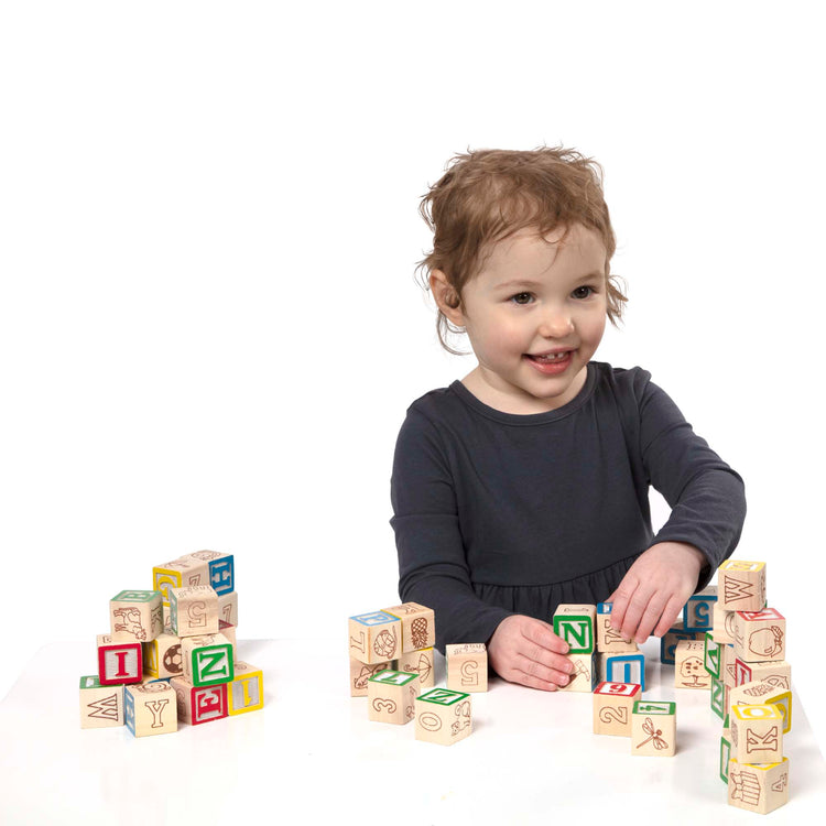 A child on white background with The Melissa & Doug Deluxe Wooden ABC/123 1-Inch Blocks Set With Storage Pouch (50 pcs)