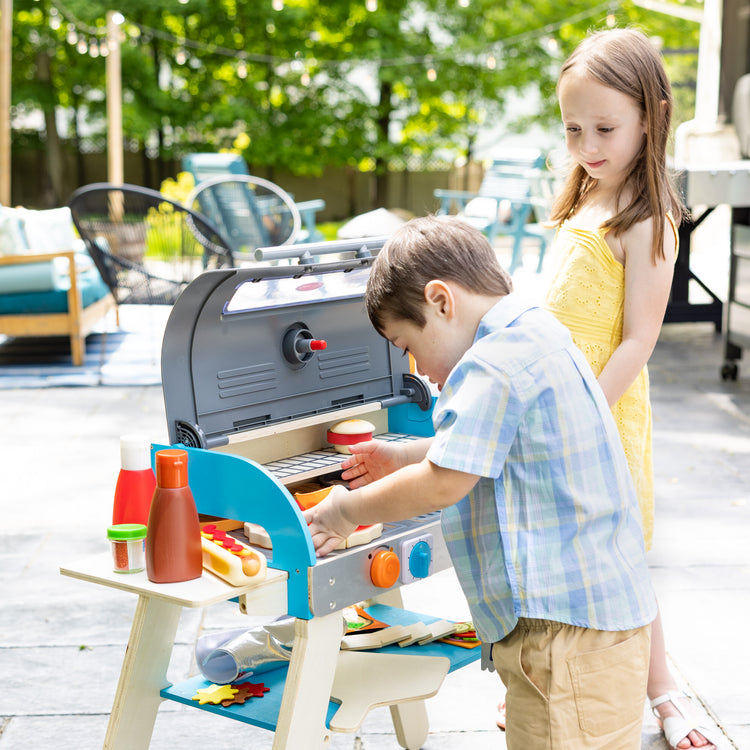 A kid playing with The Melissa & Doug Wooden Deluxe Barbecue Grill, Smoker and Pizza Oven Play Food Toy for Pretend Play Cooking for Kids