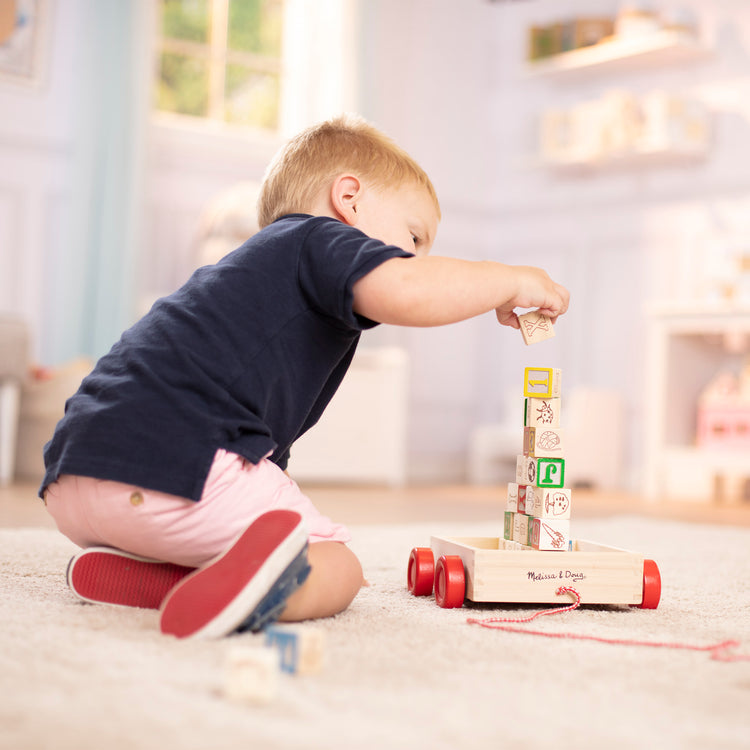 A kid playing with The Melissa & Doug Classic ABC Wooden Block Cart Educational Toy With 30 1-Inch Solid Wood Blocks