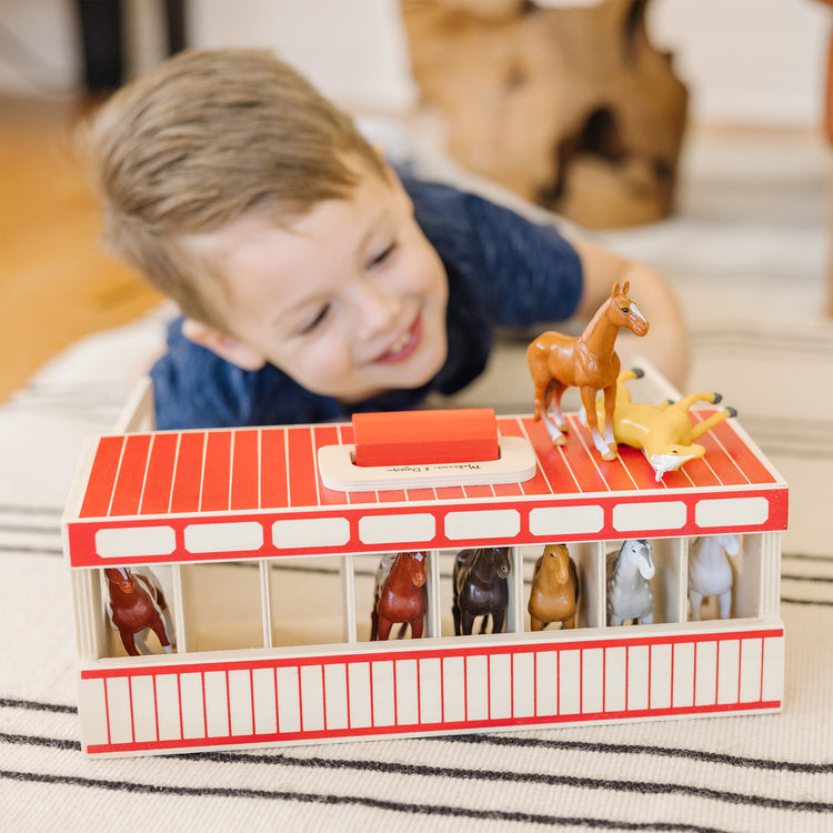 A kid playing with The Melissa & Doug Take-Along Show-Horse Stable Play Set With Wooden Stable Box and 8 Toy Horses