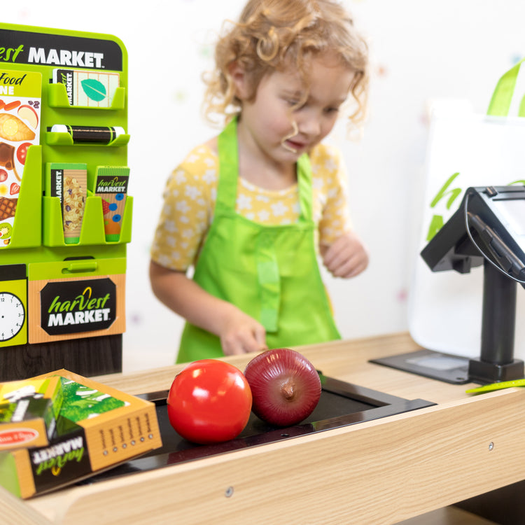 A kid playing with The Melissa & Doug Harvest Market Grocery Store and Companion Collection Accessories