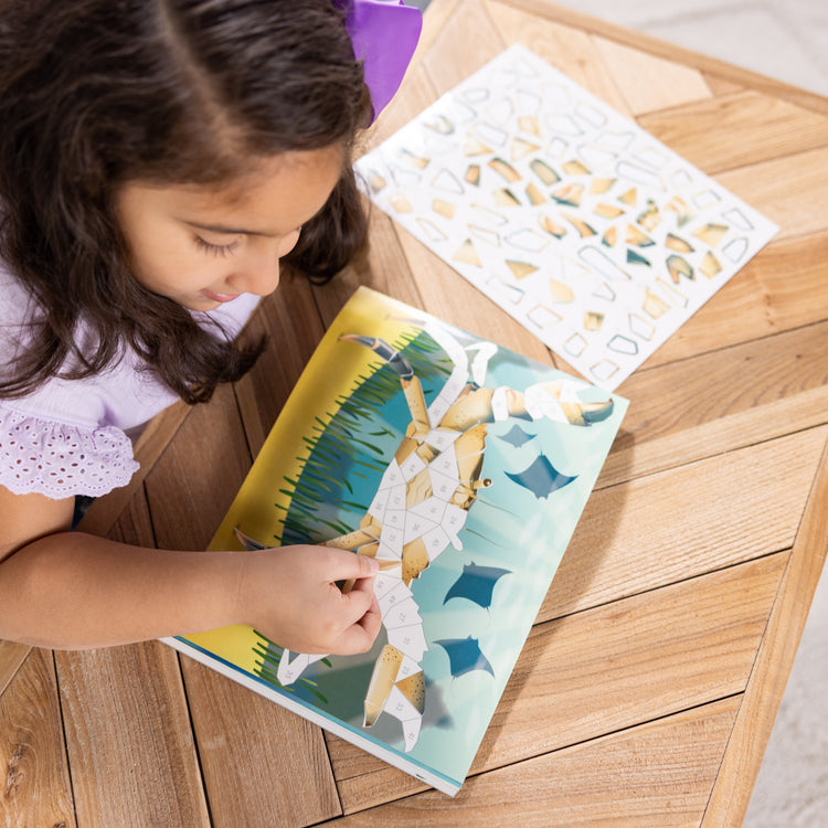 A kid playing with The Melissa & Doug Mosaic Sticker Pad Ocean Animals (12 Color Scenes to Complete with 850+ Stickers)