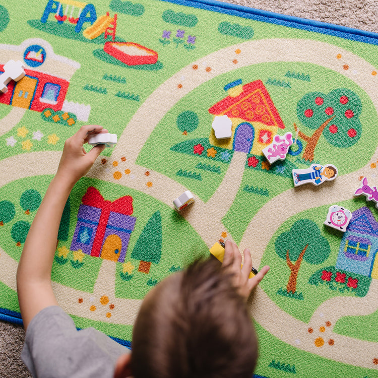 A kid playing with The Melissa & Doug Blue's Clues & You! Blue's Neighborhood Activity Rug (44 Inches x 26 Inches Rug, 9 Wooden Play Pieces)