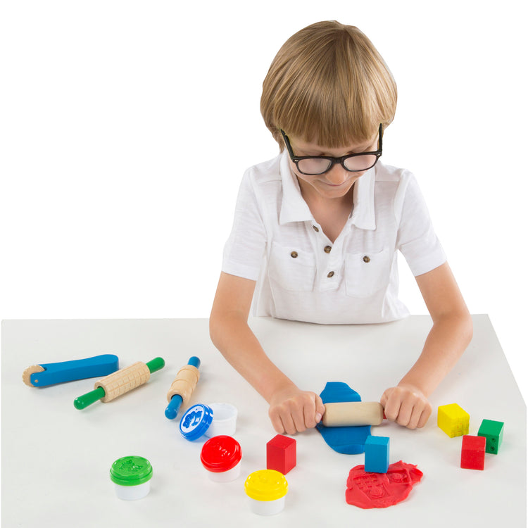 A child on white background with The Melissa & Doug Shape, Model, and Mold Craft Activity Set - 4 Tubs of Modeling Dough and Tools