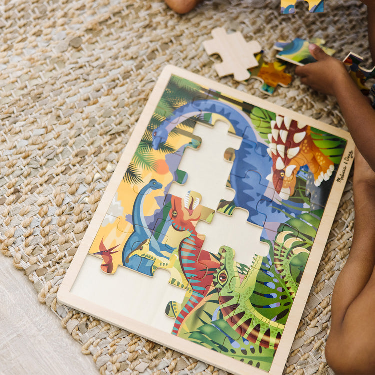 A kid playing with The Melissa & Doug Dinosaurs Wooden Jigsaw Puzzle With Storage Tray (24 pcs)