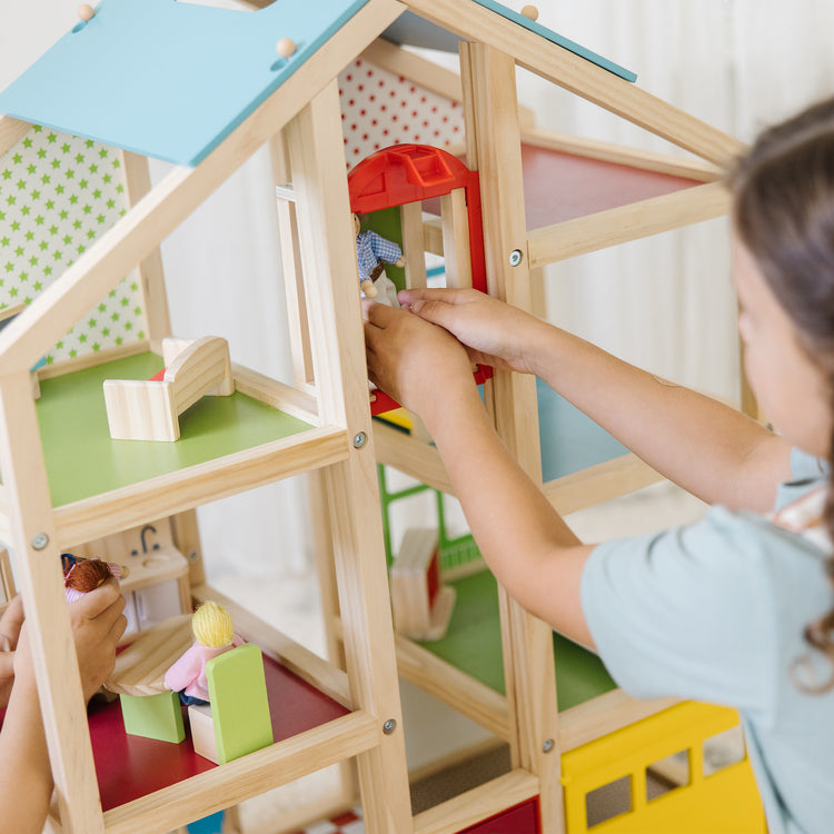 A kid playing with The Melissa & Doug Wooden Hi-Rise Dollhouse With 15 Furniture Pieces, Garage, Working Elevator