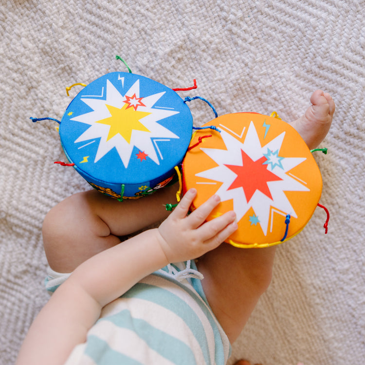 A kid playing with The Melissa & Doug K's Kids Bongo Drums Soft Musical Instrument