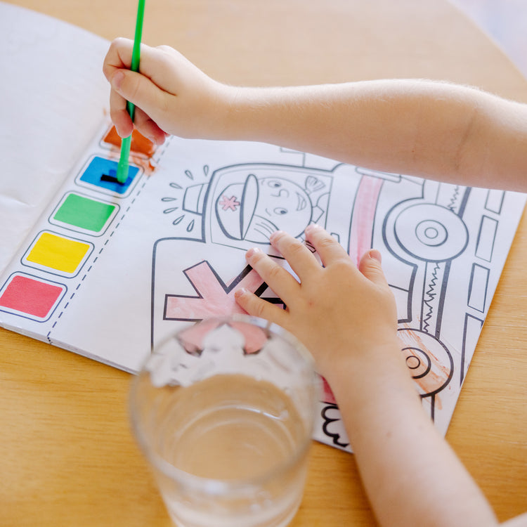 A kid playing with The Melissa & Doug Paint With Water - Vehicles, 20 Perforated Pages With Spillproof Palettes