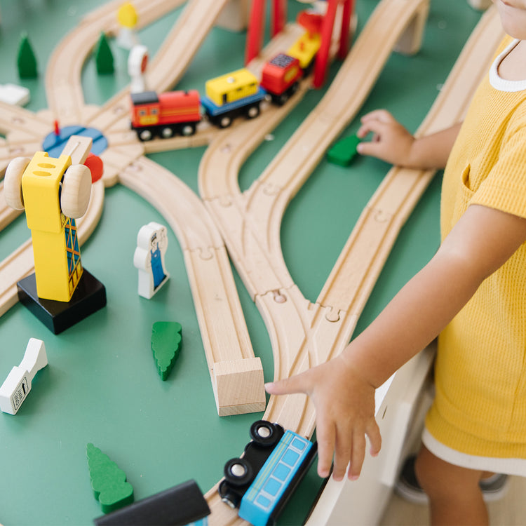 A kid playing with The Melissa & Doug Deluxe Wooden Railway Train Set (130+ pcs)