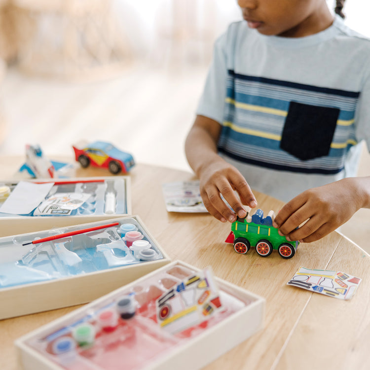 A kid playing with The Melissa & Doug Decorate-Your-Own Wooden Craft Kits 3-Pack - Plane, Train, and Race Car