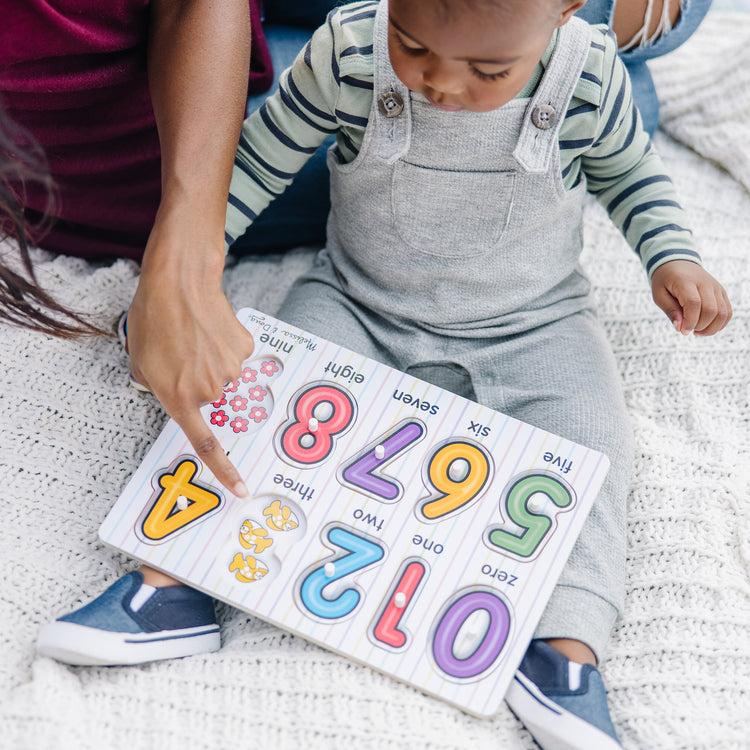 A kid playing with The Melissa & Doug Lift & See Numbers Wooden Peg Puzzle - 10 Pieces