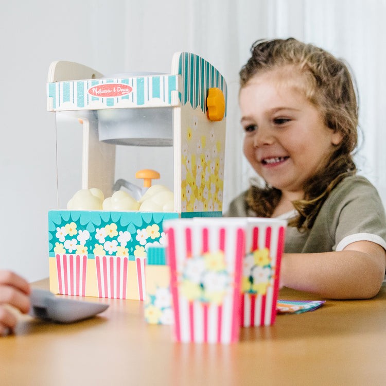 A kid playing with The Melissa & Doug Fun at the Fair! Wooden Popcorn Popping Play Food Set