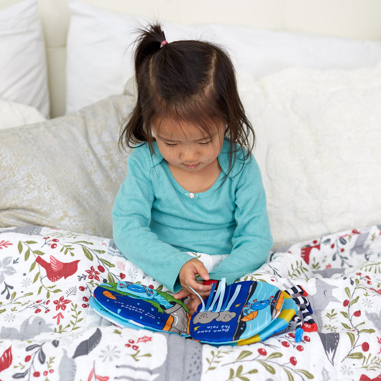 A kid playing with The Melissa & Doug K's Kids Itsy-Bitsy Spider 8-Page Soft Activity Book for Babies and Toddlers