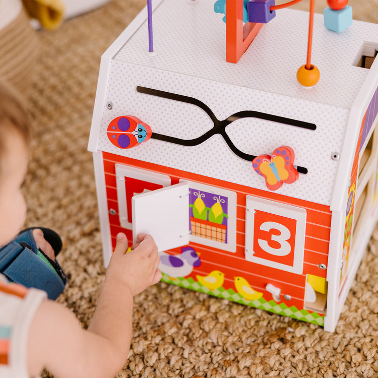 A kid playing with The Melissa & Doug First Play Slide, Sort & Roll Wooden Activity Barn with Bead Maze, 6 Wooden Play Pieces (11.75” x 11.75” x 20” Assembled)