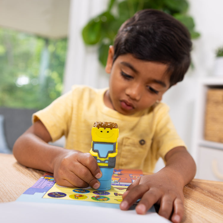 A kid playing with The Melissa & Doug Sticker WOW!™ Bulldozer Bundle: 24-Page Activity Pad, Sticker Stamper, 500 Stickers, Arts and Crafts Fidget Toy Collectible Character