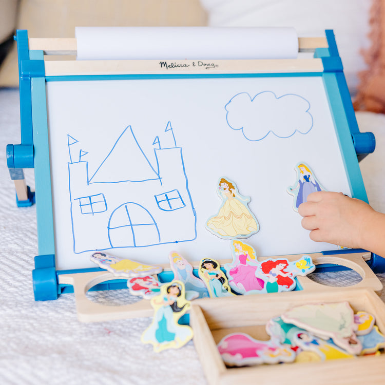 A kid playing with The Melissa & Doug Double-Sided Magnetic Tabletop Art Easel - Dry-Erase Board and Chalkboard