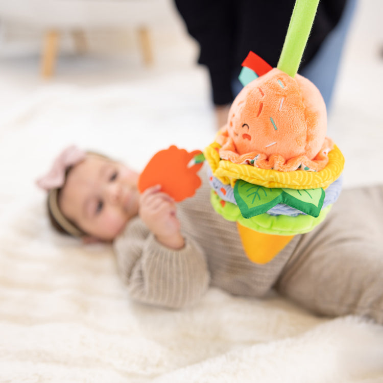 A kid playing with The Melissa & Doug Ice Cream Take-Along Clip-On Infant Toy with Sound and Vibration