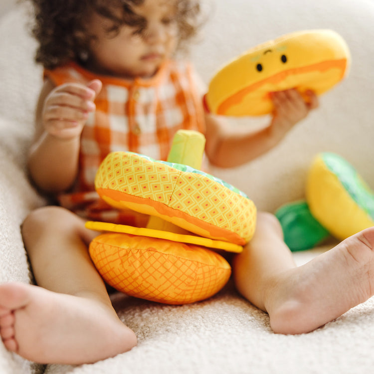 A kid playing with The Melissa & Doug Multi-Sensory Pineapple Soft Stacker Infant Toy