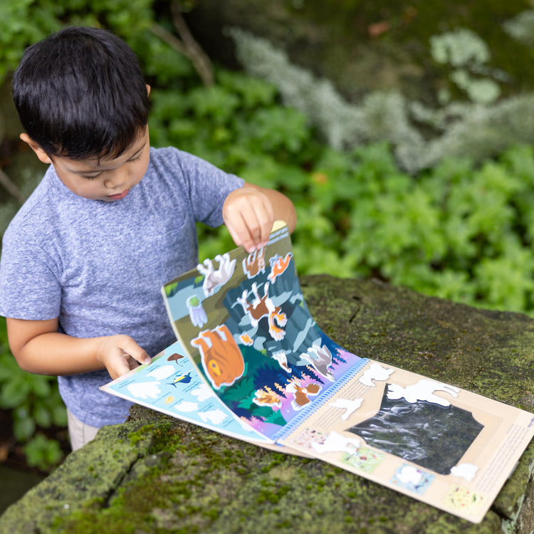 A kid playing with The Melissa & Doug National Parks Reusable Stickers Jumbo Pad: Park Animals - 5 Scenes, 121 Puffy and Cling Stickers