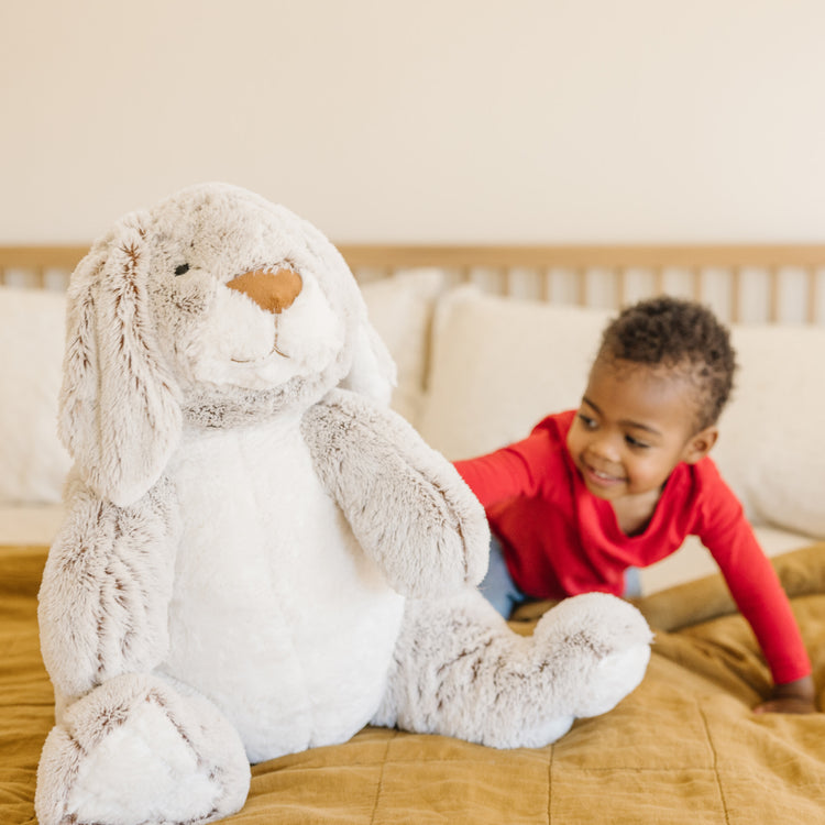 A kid playing with The Melissa & Doug Jumbo Burrow Bunny Lop-Eared Rabbit Stuffed Plush Animal (21 Inches Tall)