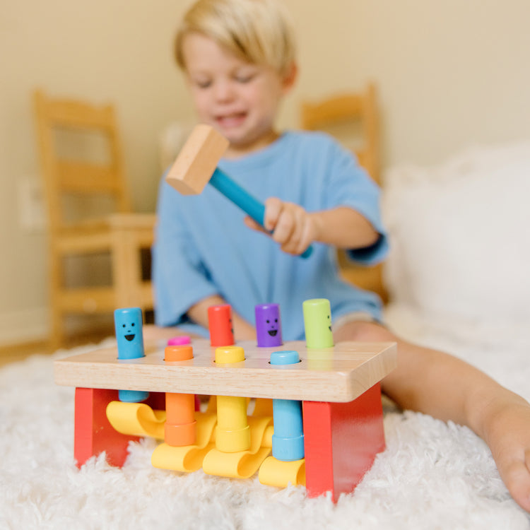 A kid playing with The Melissa & Doug Deluxe Pounding Bench Wooden Preschool Learning Toy With Mallet