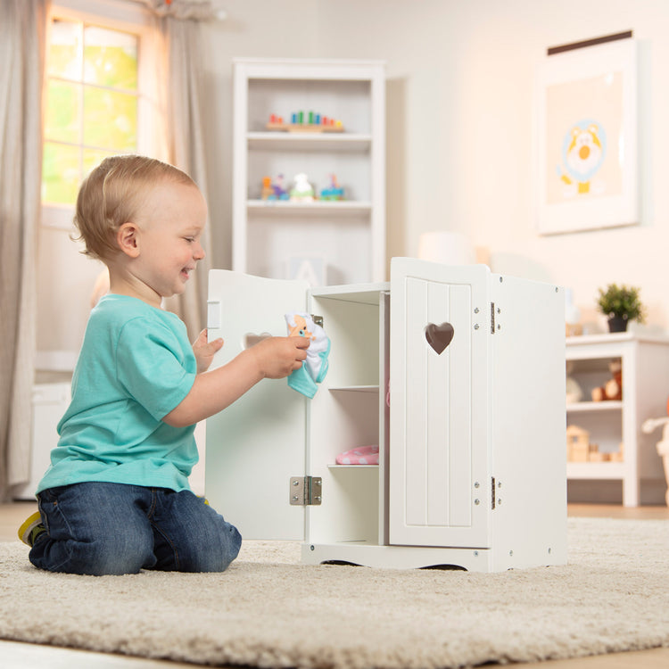 A kid playing with The Melissa & Doug Mine to Love Wooden Play Armoire Closet for Dolls, Stuffed Animals - White (17.3”H x 12.4”W x 8.5”D Assembled)