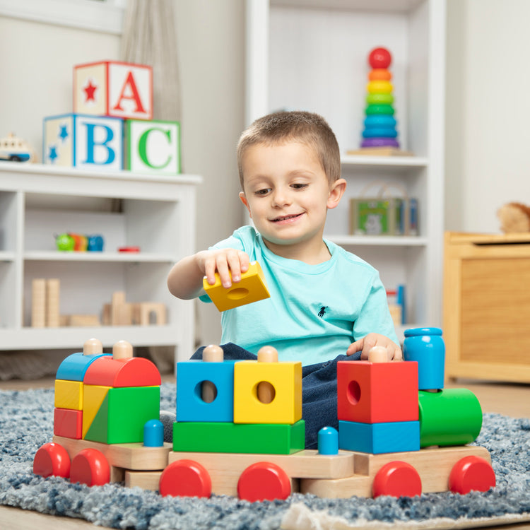 A kid playing with The Melissa & Doug Wooden Jumbo Stacking Train – 4-Color Classic Wooden Toddler Toy (17 pcs)