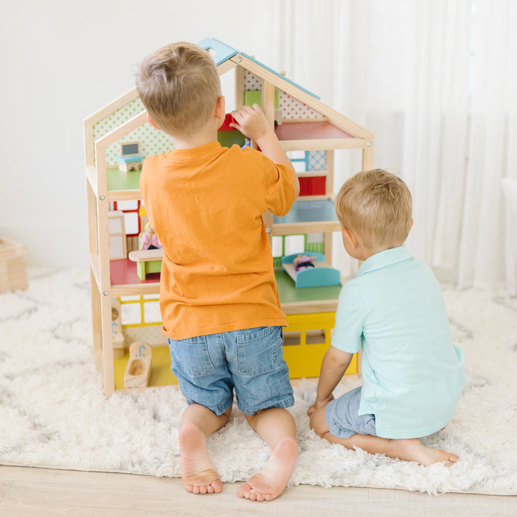 A kid playing with The Melissa & Doug Wooden Hi-Rise Dollhouse With 15 Furniture Pieces, Garage, Working Elevator