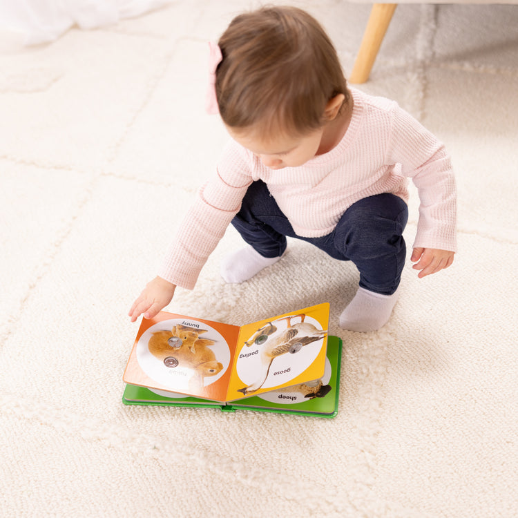 A kid playing with The Melissa & Doug Children’s Book – Poke-a-Dot: Farm Animal Families (Board Book with Buttons to Pop)