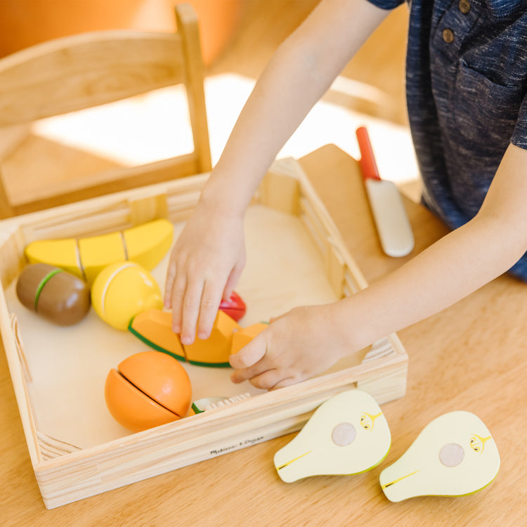 A kid playing with The Melissa & Doug Cutting Fruit Set - Wooden Play Food Kitchen Accessory, Multi