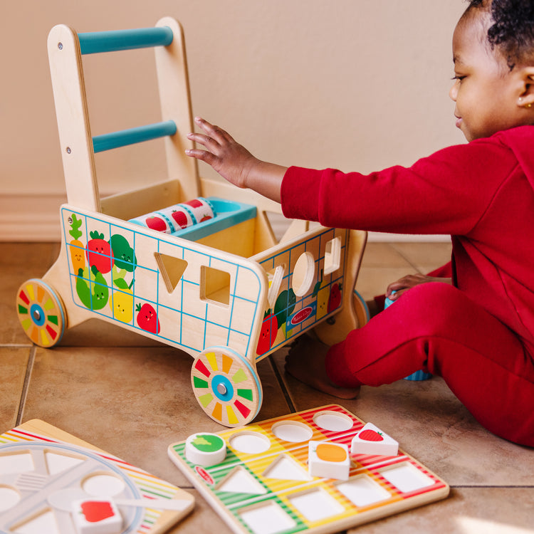 A kid playing with The Melissa & Doug Wooden Shape Sorting Grocery Cart Push Toy and Puzzles