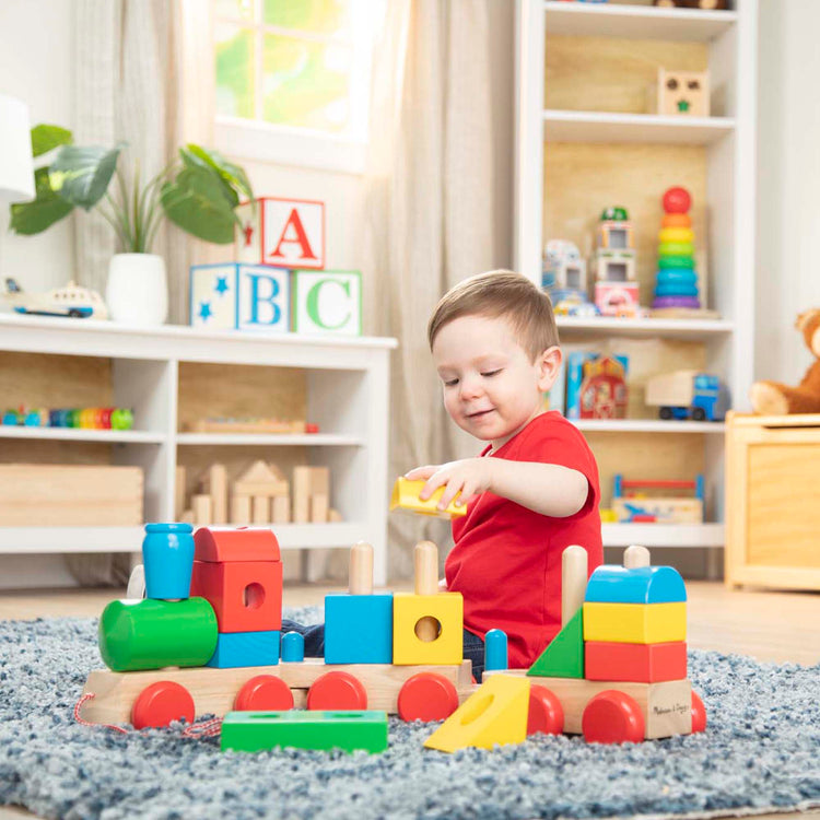 A kid playing with The Melissa & Doug Wooden Jumbo Stacking Train – 4-Color Classic Wooden Toddler Toy (17 pcs)