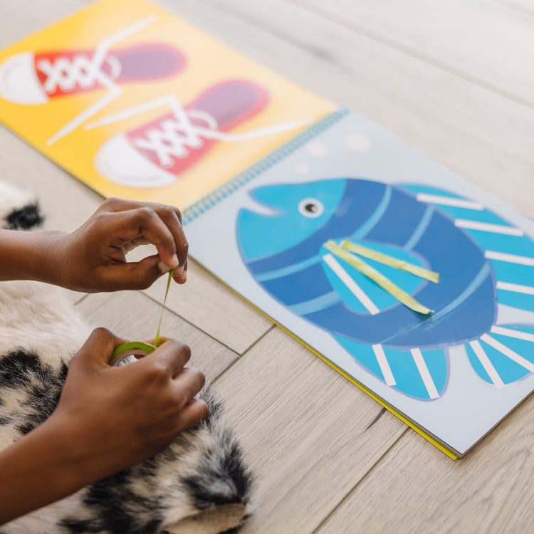 A kid playing with The Melissa & Doug Tape Activity Book: 4 Rolls of Easy-Tear Tape and 20 Reusable Scenes