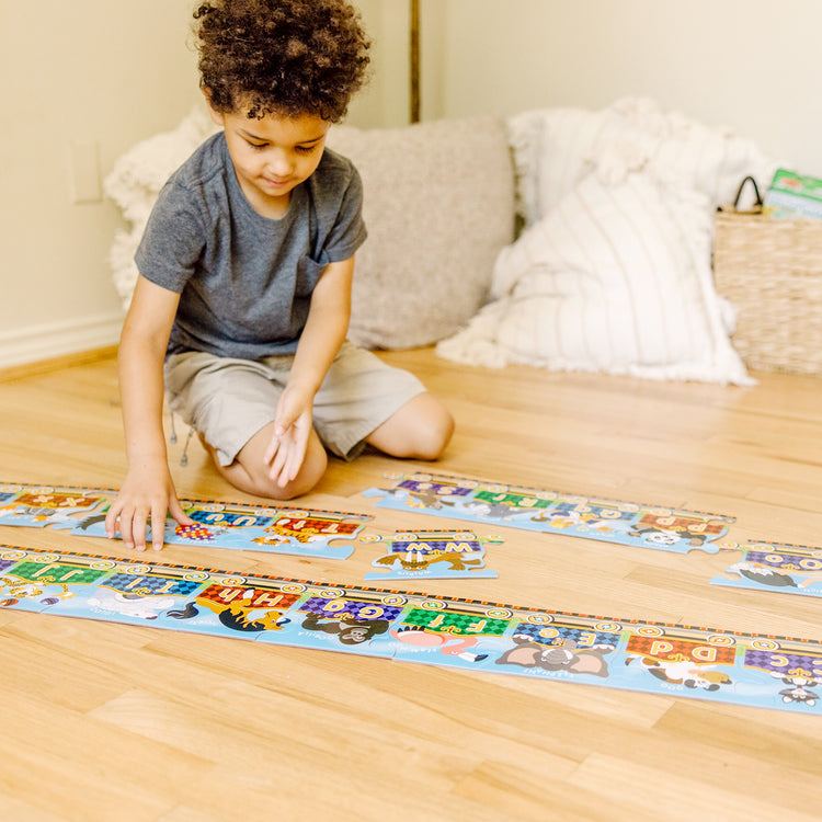 A kid playing with The Melissa & Doug Alphabet Express Jumbo Jigsaw Floor Puzzle (27 pcs, 10 feet long)