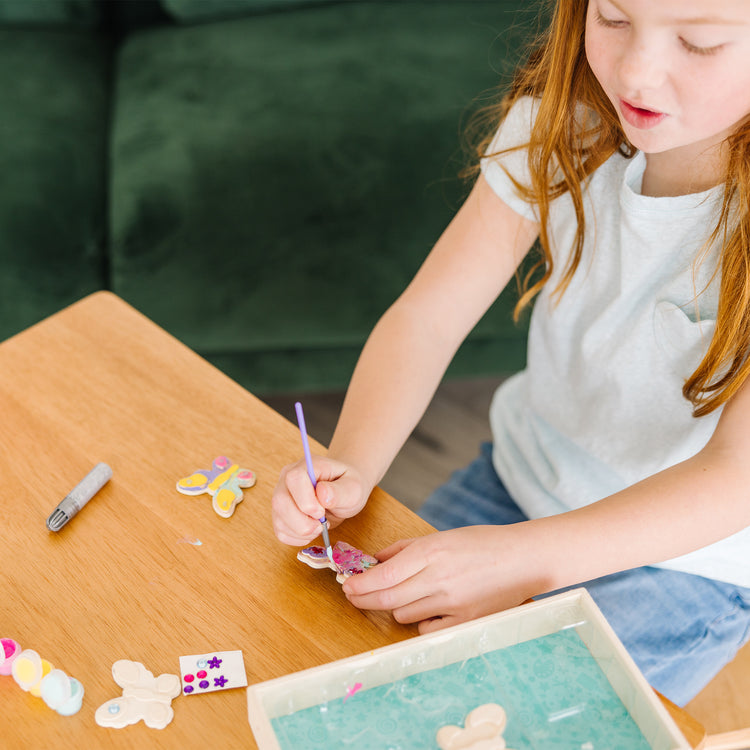 A kid playing with The Melissa & Doug Created by Me! Wooden Butterfly Magnets Craft Kit (4 Designs, 4 Paints, Stickers, Glitter Glue)