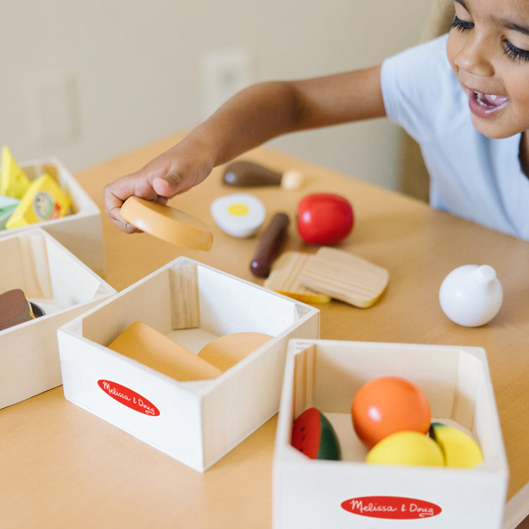 A kid playing with The Melissa & Doug Food Groups - 21 Wooden Pieces and 4 Crates, Multi