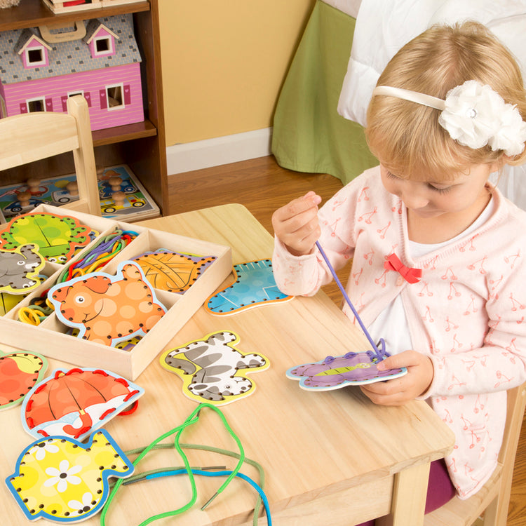 A kid playing with The Melissa & Doug Alphabet Wooden Lacing Cards With Double-Sided Panels and Matching Laces