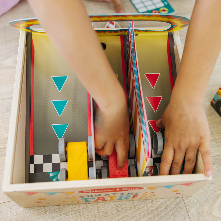 A kid playing with The Melissa & Doug Fun at the Fair! Wooden Ring of Fire Stunt Jumper Cars Game