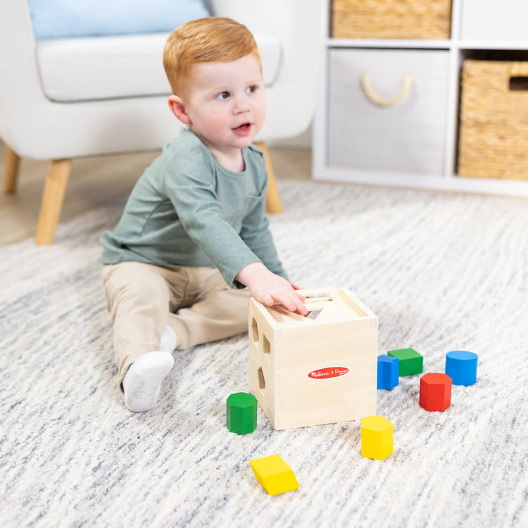 A kid playing with The Melissa & Doug Shape Sorting Cube - Classic Wooden Toy With 12 Shapes