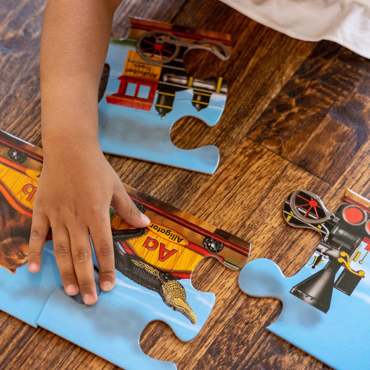 A kid playing with The Melissa & Doug Alphabet Train Jumbo Jigsaw Floor Puzzle - Letters and Animals (28 pcs, 10 feet long)