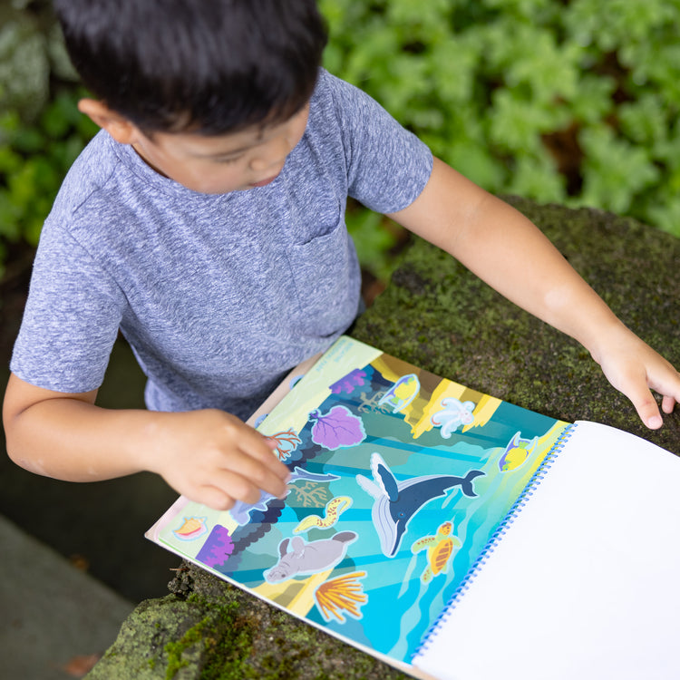 A kid playing with The Melissa & Doug National Parks Reusable Stickers Jumbo Pad: Park Animals - 5 Scenes, 121 Puffy and Cling Stickers