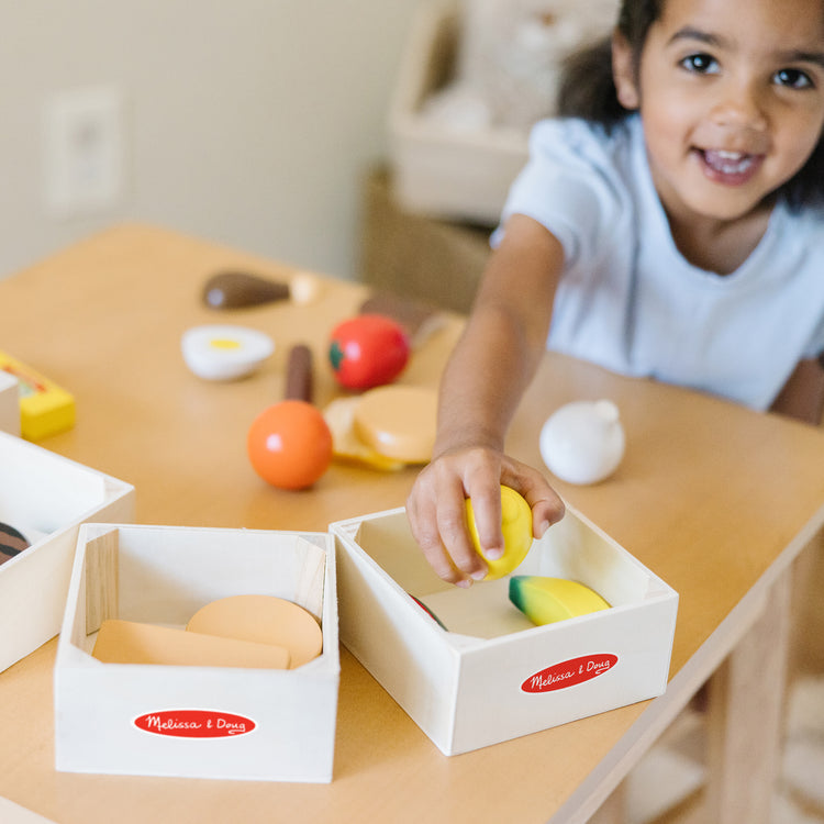 A kid playing with The Melissa & Doug Food Groups - 21 Wooden Pieces and 4 Crates, Multi