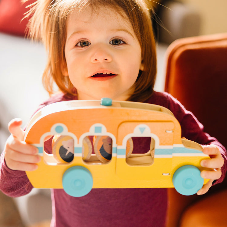 A kid playing with The Melissa & Doug GO Tots Wooden Roll & Ride Bus with 3 Disks