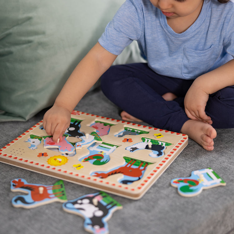 A kid playing with The Melissa & Doug Farm Animals Sound Puzzle - Wooden Peg Puzzle With Sound Effects (8 pcs)