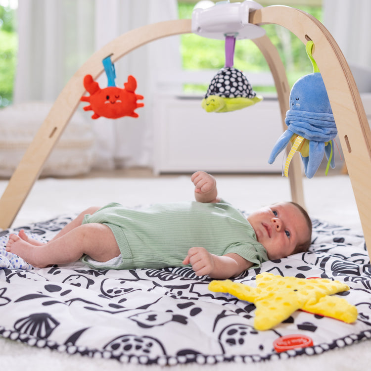 A kid playing with The Melissa & Doug Ocean Easy-Fold Play Gym Developmental Toy for Infants, Reversible Mar, 5 Soft Toys, Birth to 9 Months