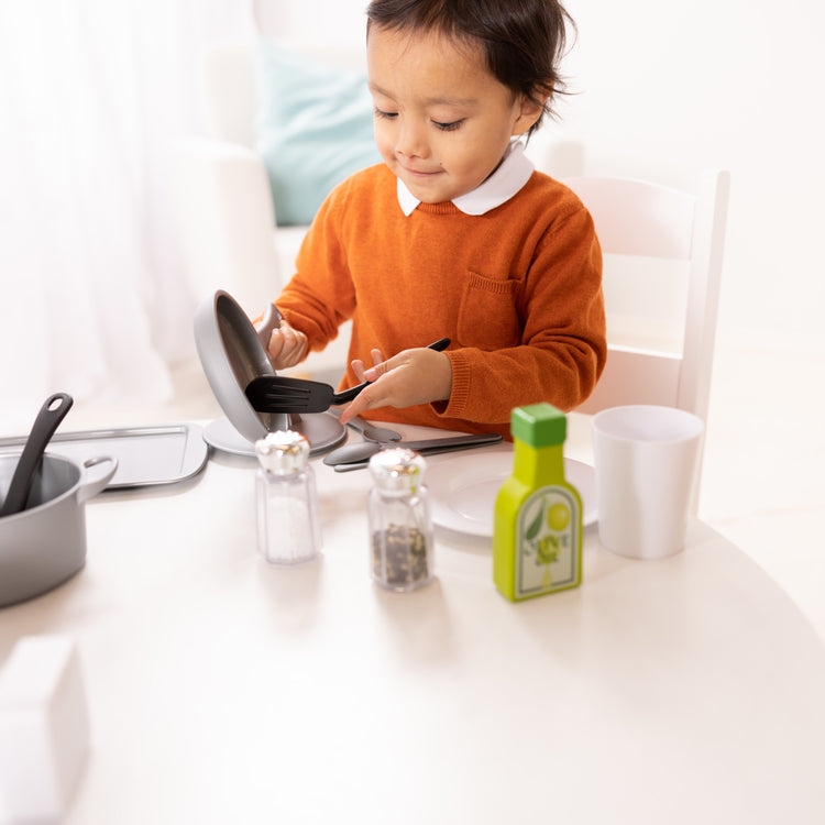 A kid playing with The Melissa & Doug 22-Piece Play Kitchen Accessories Set - Utensils, Pot, Pans, and More