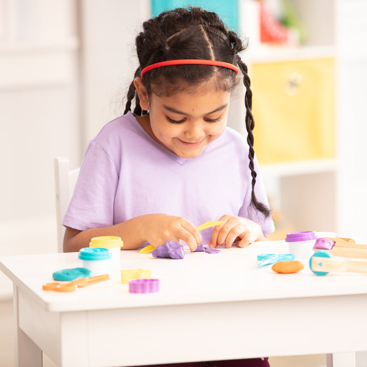 A kid playing with The Melissa & Doug Clay Play Activity Set - With Sculpting Tools and 8 Tubs of Modeling Dough