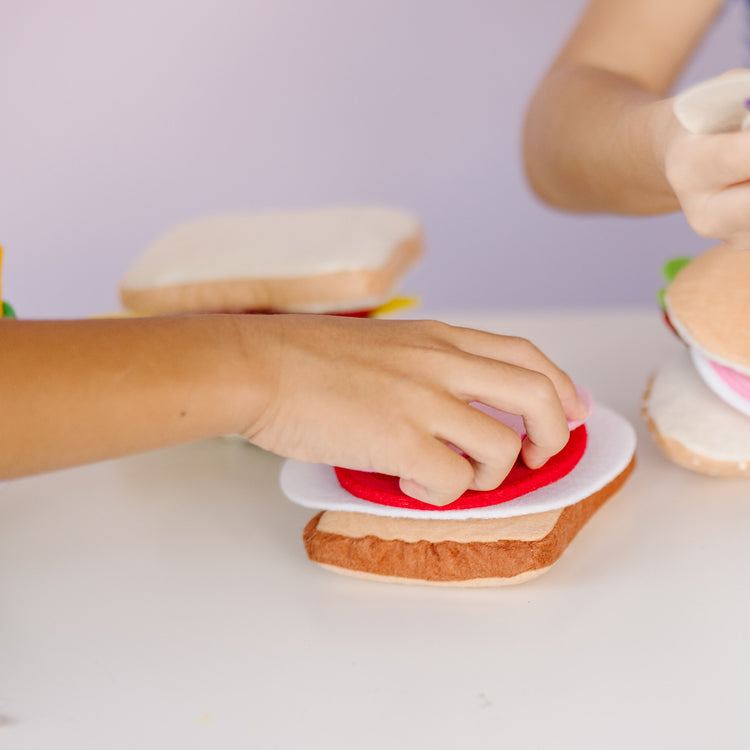 A kid playing with The Melissa & Doug Felt Food Sandwich Play Food Set (33 pcs)