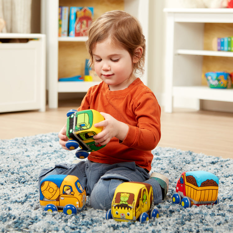 A kid playing with The Melissa & Doug Pull-Back Construction Vehicles - Soft Baby Toy Play Set of 4 Vehicles